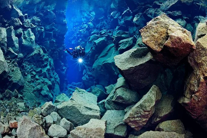 Ein Taucher mit Lampe zwischen riesigen Lavablöcken in blauem Wasser