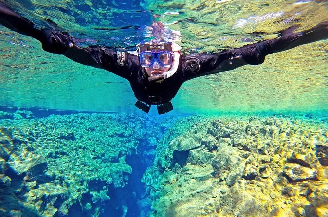 A snorkeler in a drysuit and mask spreading their arms above the lava floor