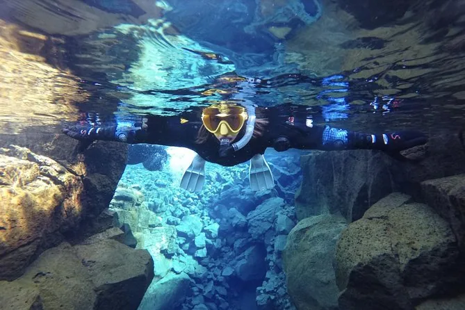 A snorkeler in a drysuit and yellow mask floating through a narrow blue crack
